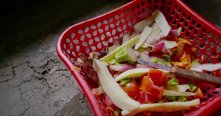 Hand picking up a red basket with leftover vegetables
