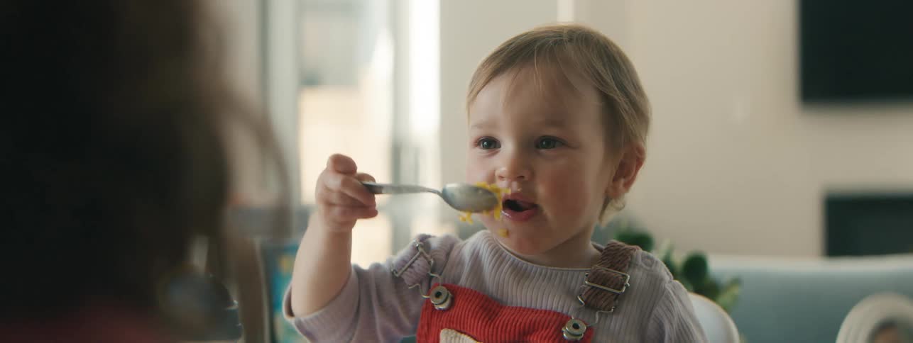Little girl sitting at the table holding a spoon and eating