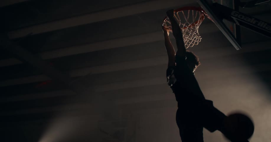 Silhouette of a young man jumping and throwing the ball into the basketball hoop