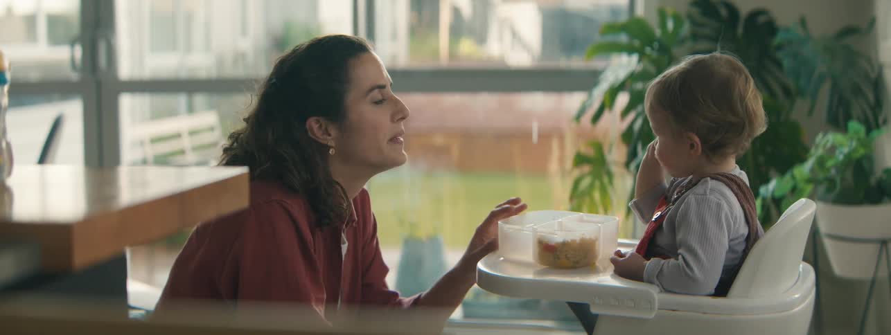 Mother crouched down watching her little daughter eat