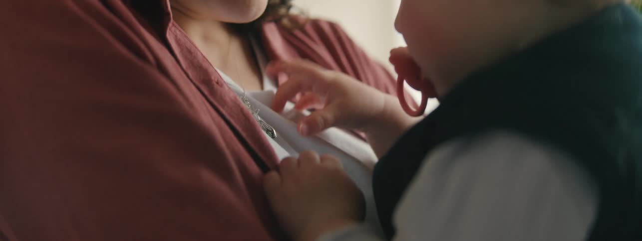 A woman with curly hair wearing a reddishbrown shirt gazing down intently at a child suggesting a moment of connection or care