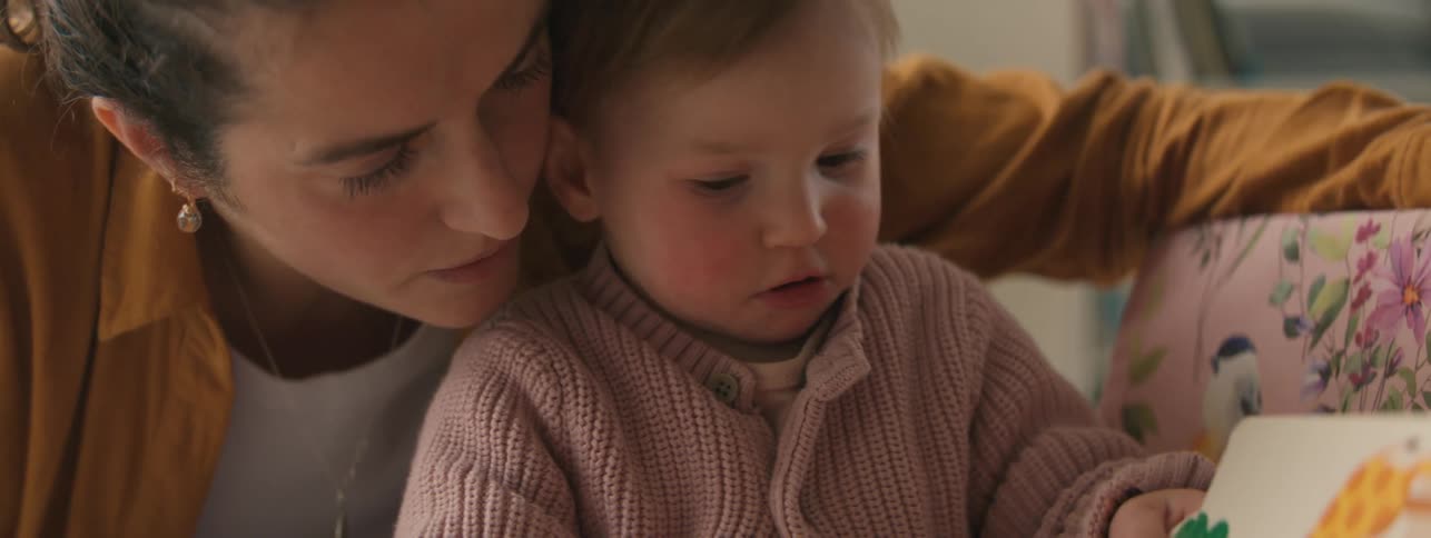 Mother crouching down interacting with her young daughter who is holding a book