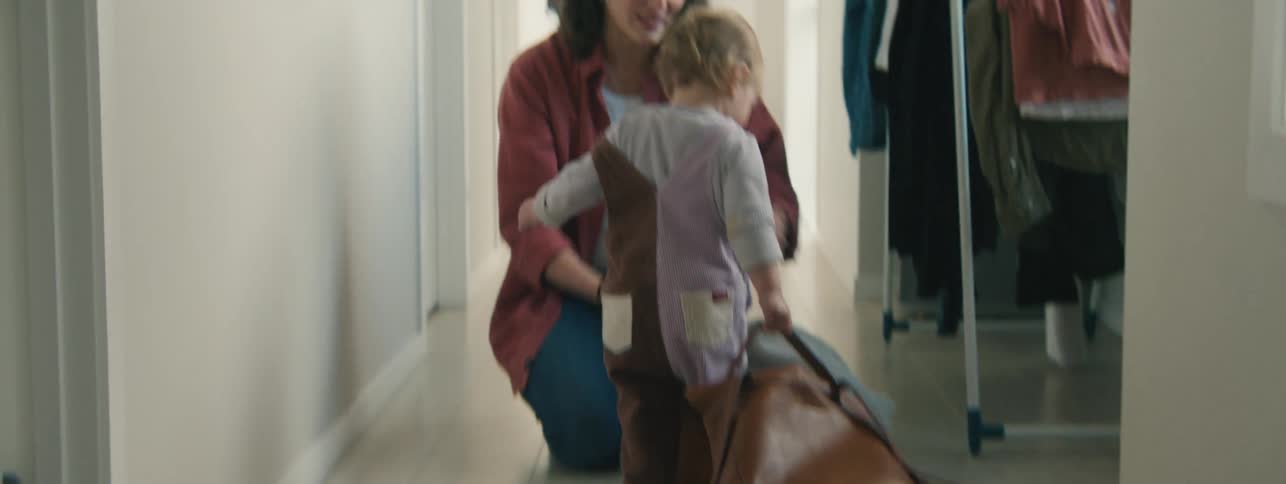 Little girl dragging a brown leather bag towards her mother