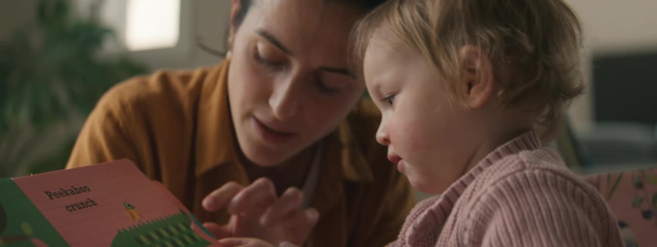 A mother and child read a book with colorful illustrations at home