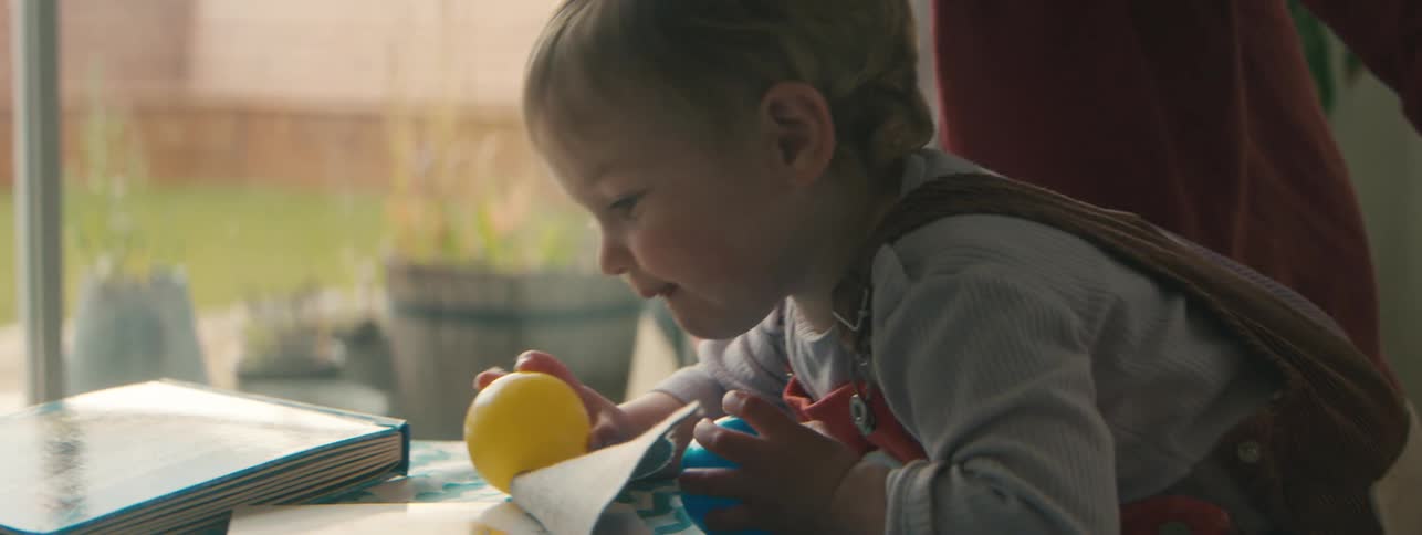 A toddler runs into a room holding plastic balls and then plays with his mother