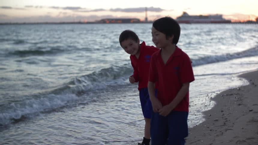 Two boys walk on the beach at dusk