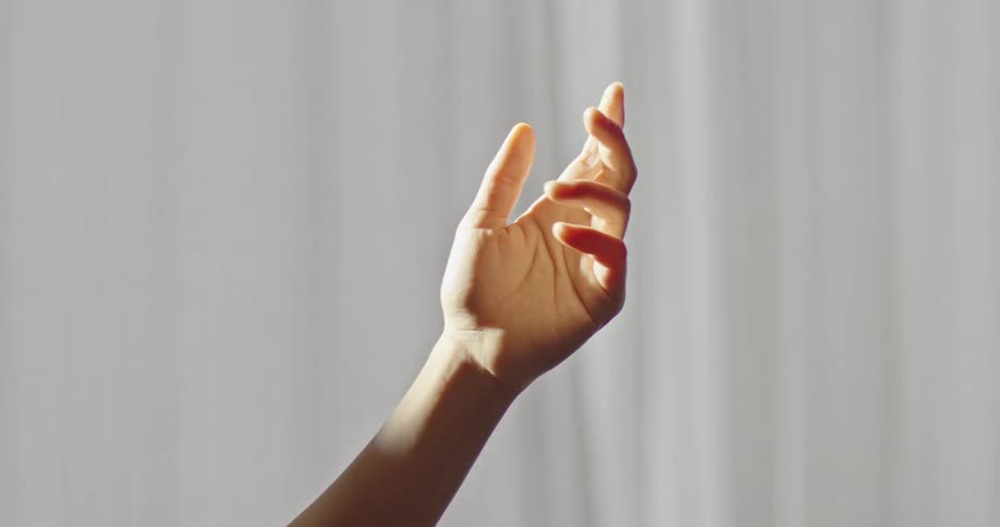 A hand reaching up to meet the sunlight in front of white curtains