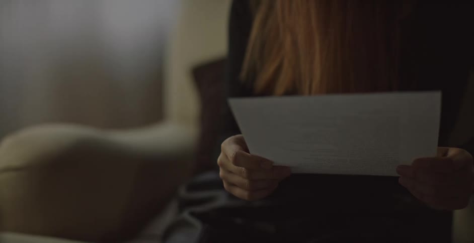 A woman is reading a paper on the chair