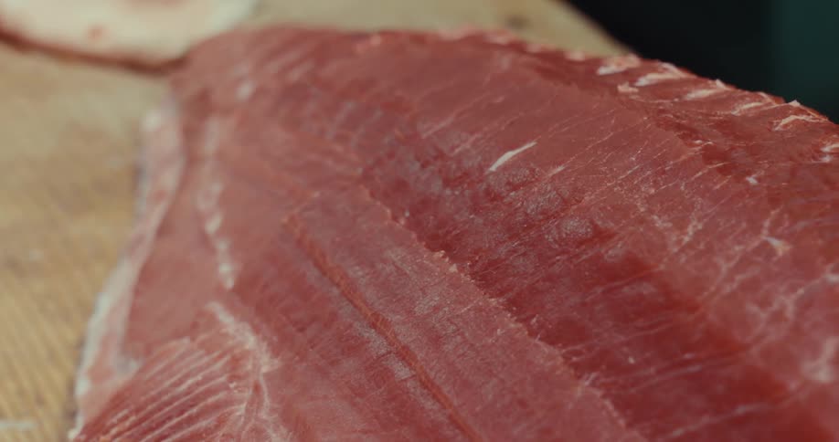 Close up of a knife slicing a piece of raw tuna on a wooden cutting board