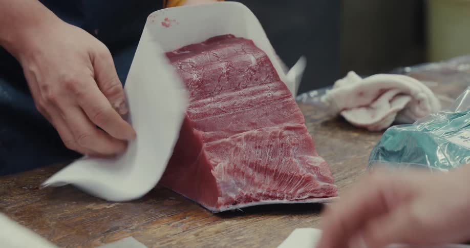 A fishmonger wrapping a large slab of tuna