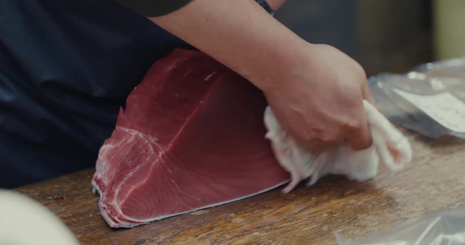 A persons hand is wiping a large piece of raw tuna with a cloth