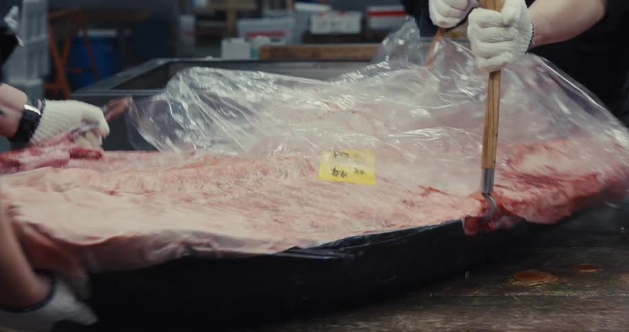 Three people wearing gloves moving a piece of fresh tuna on a table
