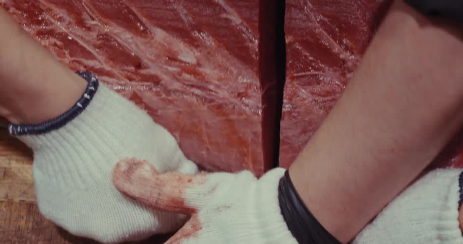 A couple of butchers cutting a large raw tuna steak with a sharp knife