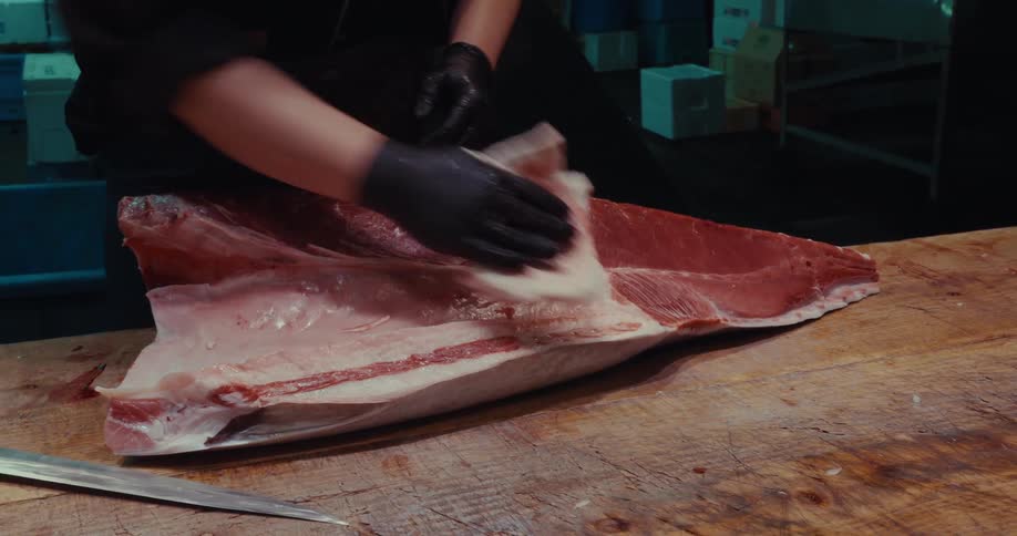 Hand with gloves cleaning a piece of tuna on top of a wooden table