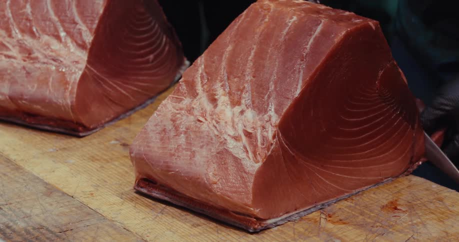 Workers wipe down and trim large chunks of raw fish