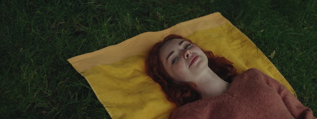 Redhead woman lying on a yellow towel on the grass during the day