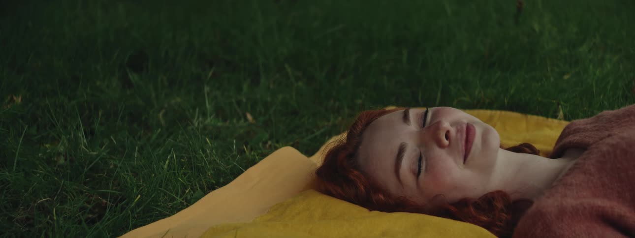 Closeup of a beautiful redhead womans face resting on a yellow blanket over green grass