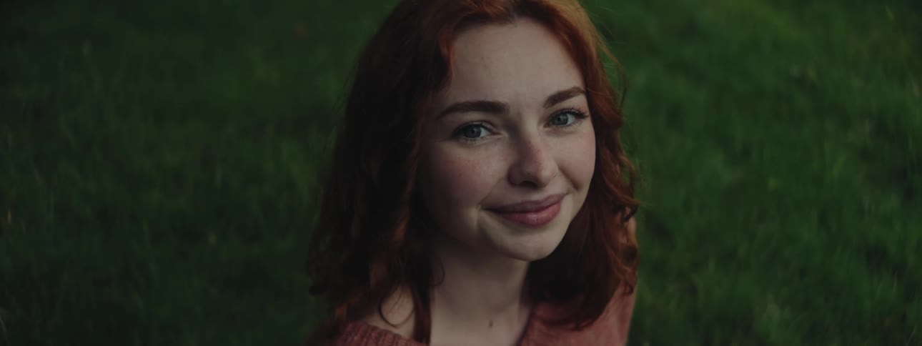A woman with red hair looks up and smiles slightly