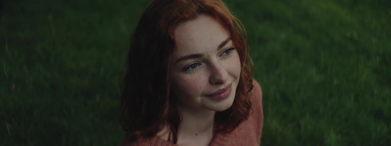 Portrait of a redhaired woman with a happy facial expression sitting on the grass