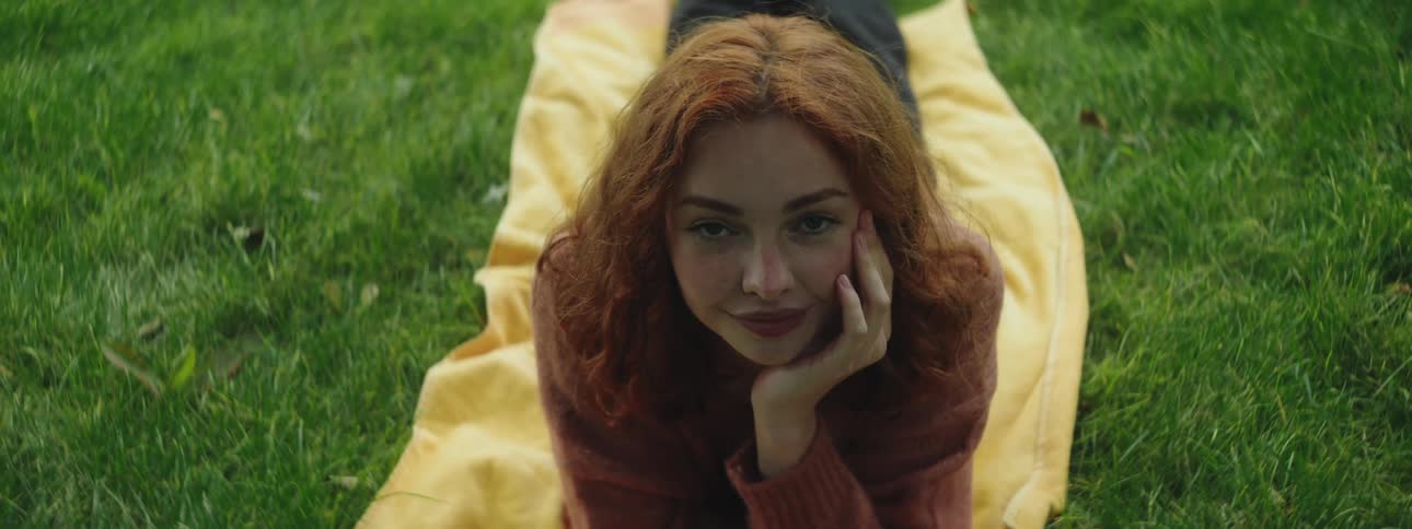 Closeup of a beautiful redhead womans face resting on a yellow blanket over green grass