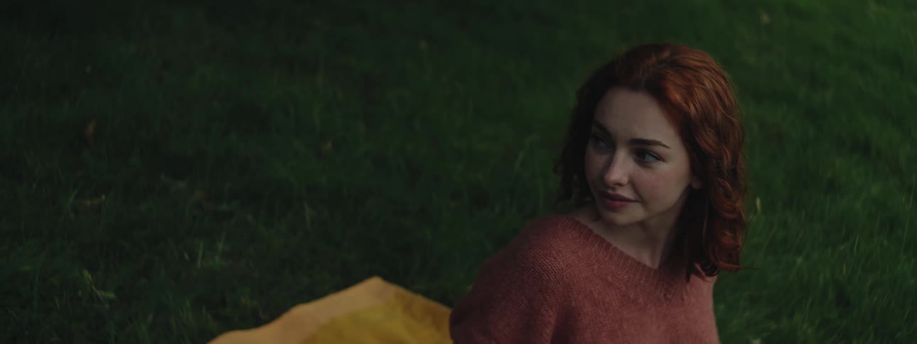 Redhead woman sitting on grass looking away smiling