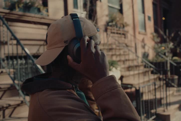 A young man stands on a city street putting on headphones to listen to music