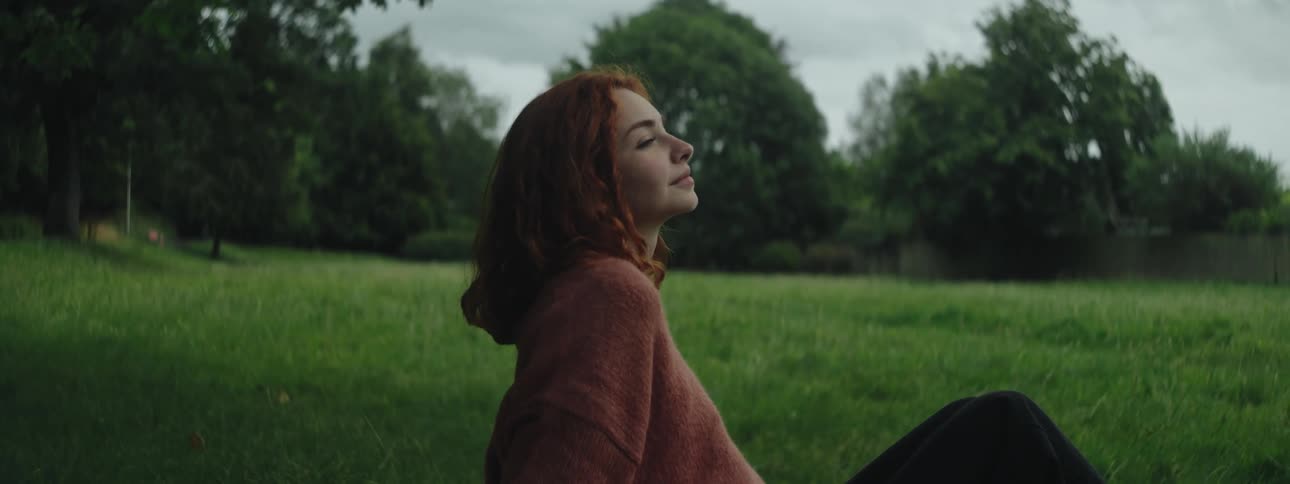 Redhead woman sitting on the grass thoughtfully