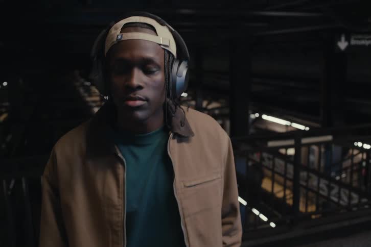 Portrait of a man with headphones walking through a subway station at night