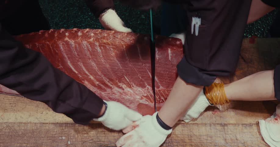 Two people holding a large tuna fish so a third person can cut off a thick slice