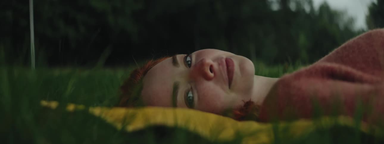 Redheaded woman turning her face away while lying on a yellow towel on the grass