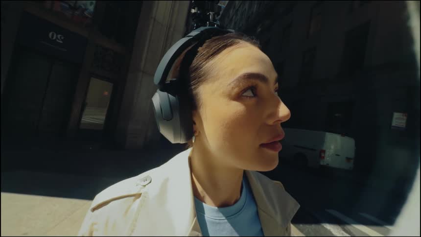 Portrait of a young woman with headphones on the sidewalk at the edge of a busy street