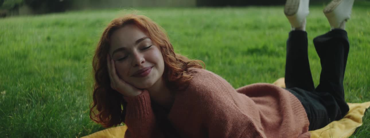 Smiling redhead woman lying with her feet up on a rug in the grass