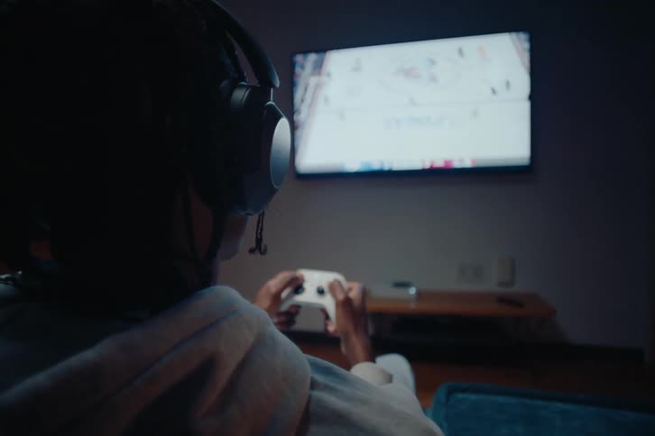 Back view of a man with headphones playing video games in his bedroom