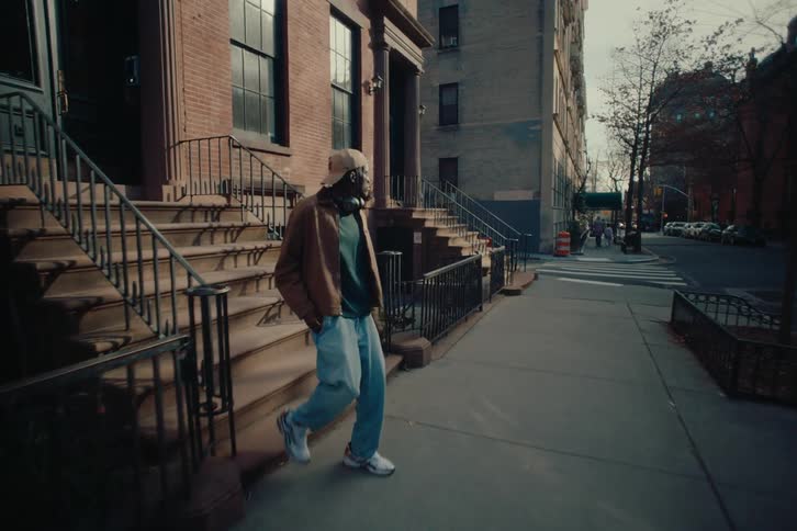 Man wearing headphones walks down the apartment steps and stops on the sidewalk to use his smartphone