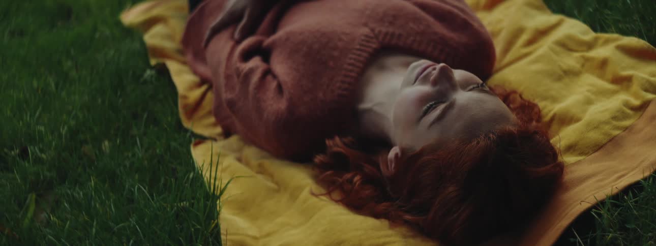 Red headed woman lying on a blanket on the grass smiles