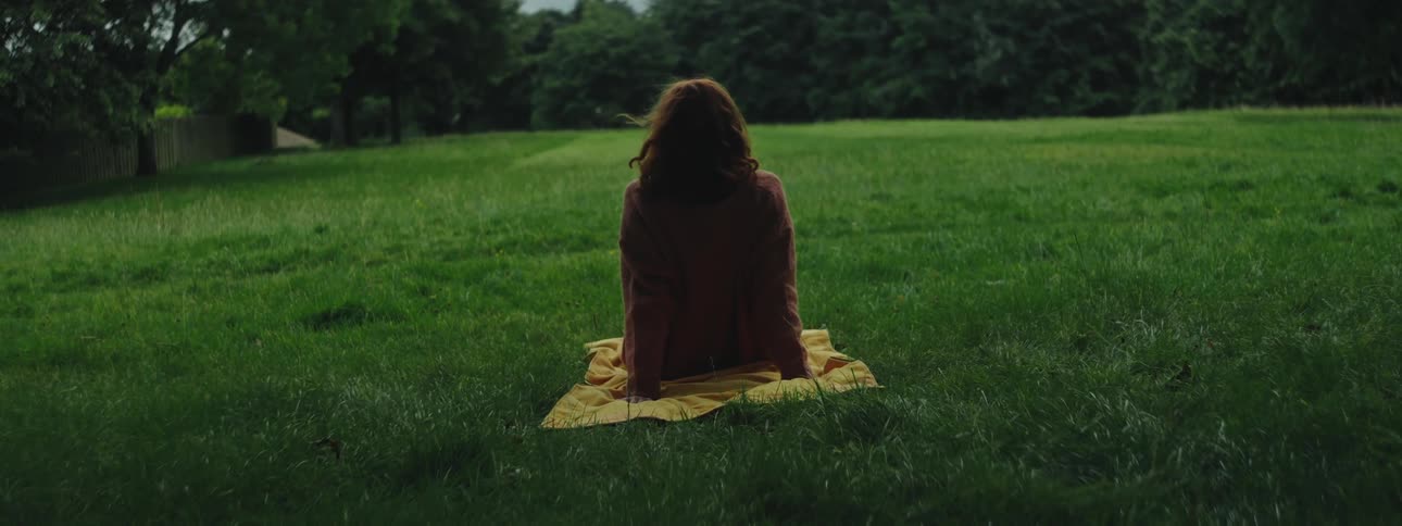 Woman sitting in a field with grass and trees around