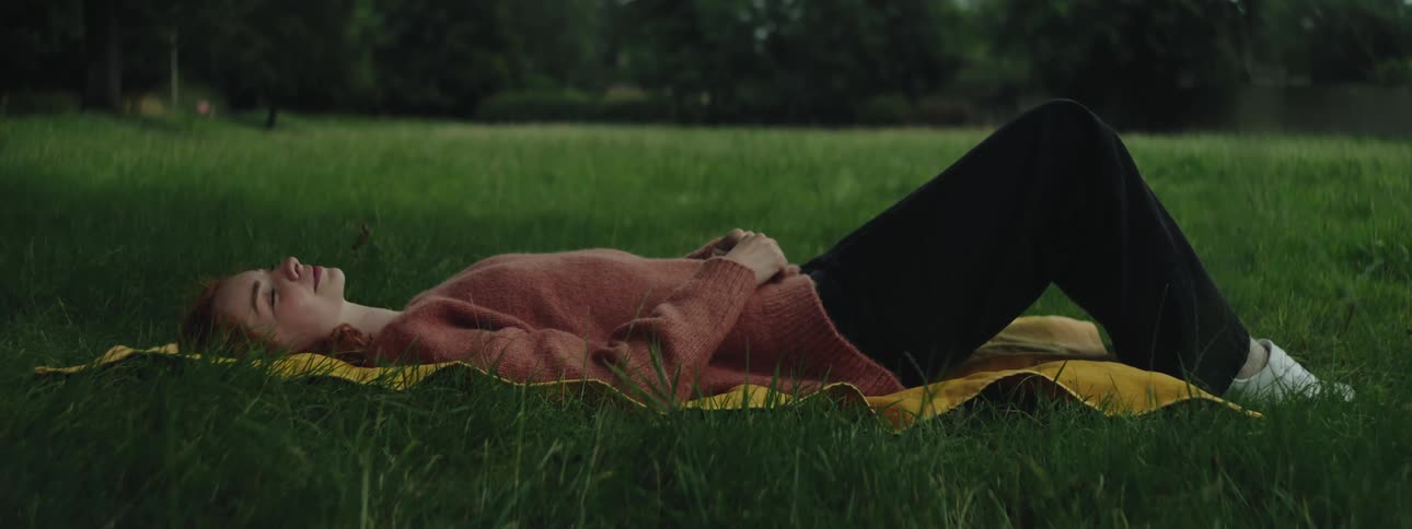 Woman relaxes by lying on a blanket on the grass during the day