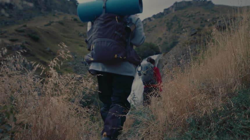 Two people with backpacks walking between mountains