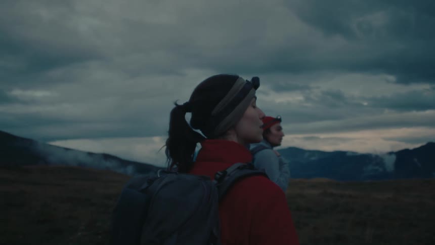 A young couple with backpacks hikes on plains near mountains under cloudy skies at dusk
