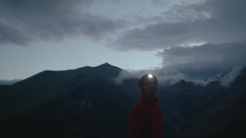 Woman with a flashlight on her head enjoying the view of mountain ranges at dusk