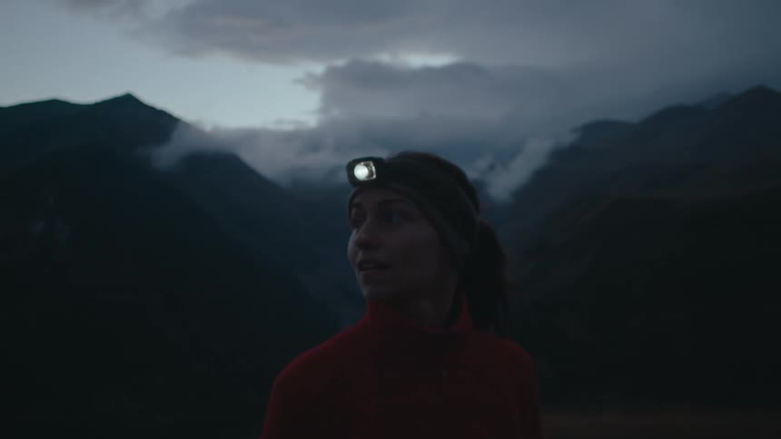 Woman hiker with a headlamp enjoys the view of mountain ranges on a cloudy morning