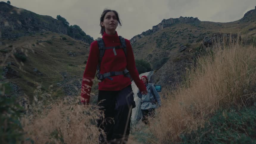 Woman and a man with backpacks walking through the mountains with a waterfall in the background