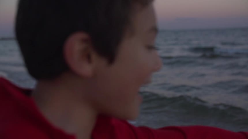 Two children standing on the shore at sunset smiling