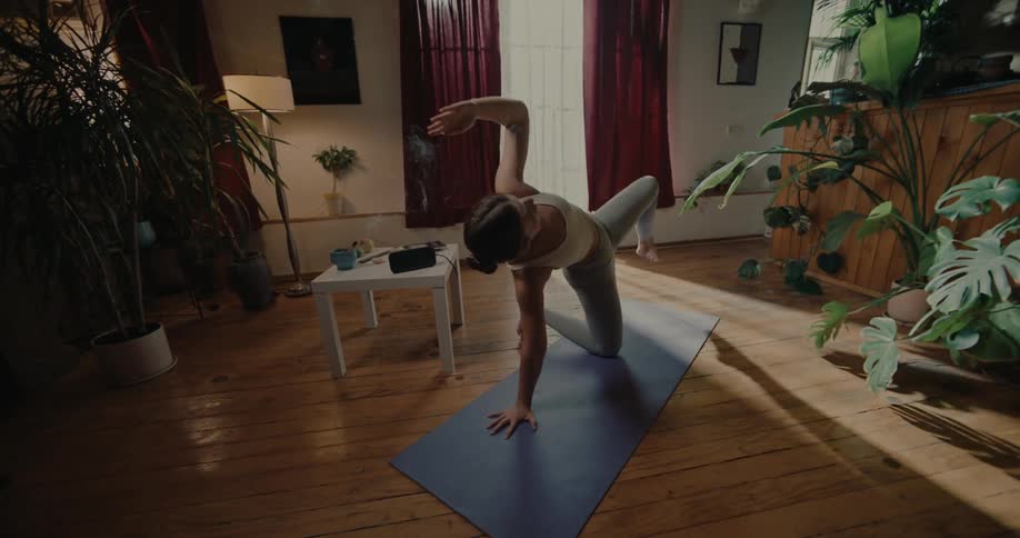 A young woman does arm and leg stretches on a yoga mat inside of a house
