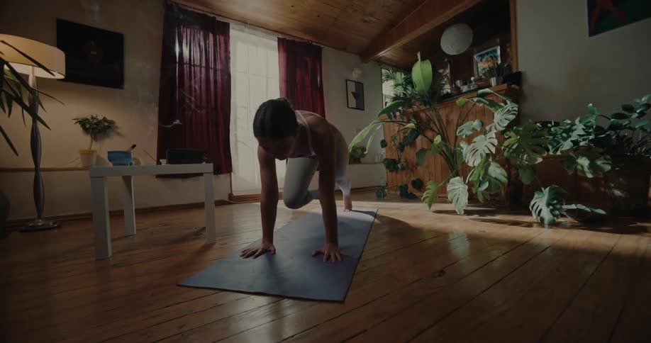 A white woman in workout gear does a cardiostretching type activity on a mat in a living room