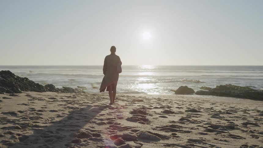 Woman walking on the sand of the beach towards the sea