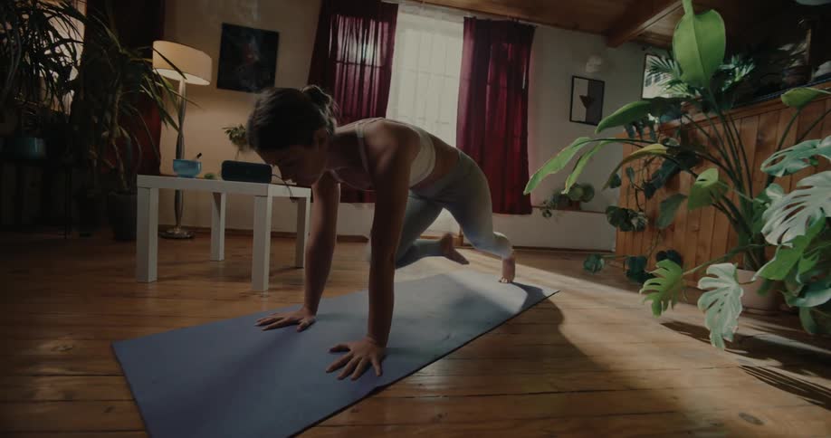 A young woman does cardio exercises on a yoga mat in a living room