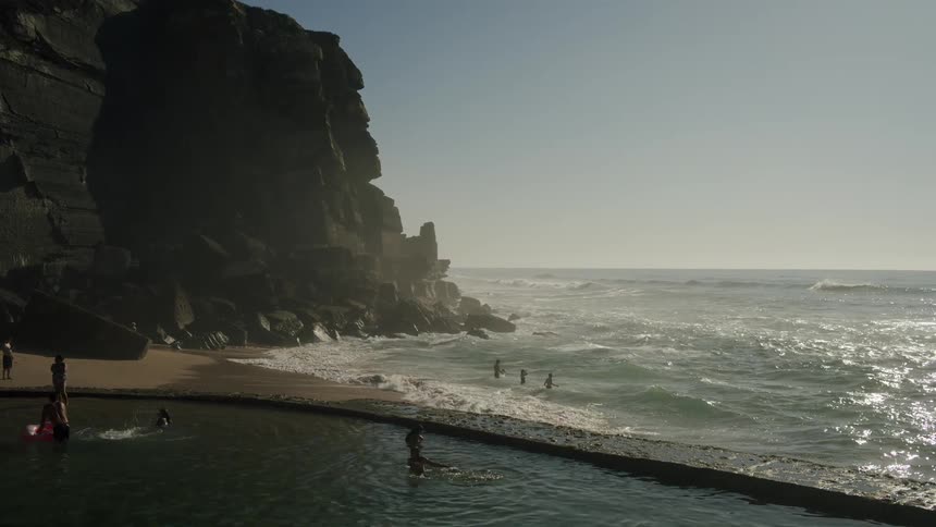 People playing in the water in the ocean in front of a mountain