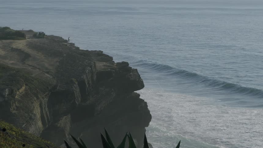 Waves crash against the shore of the cliff