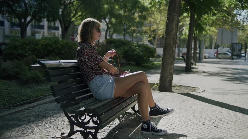 Woman sitting in a public square rummaging through her bag in broad daylight
